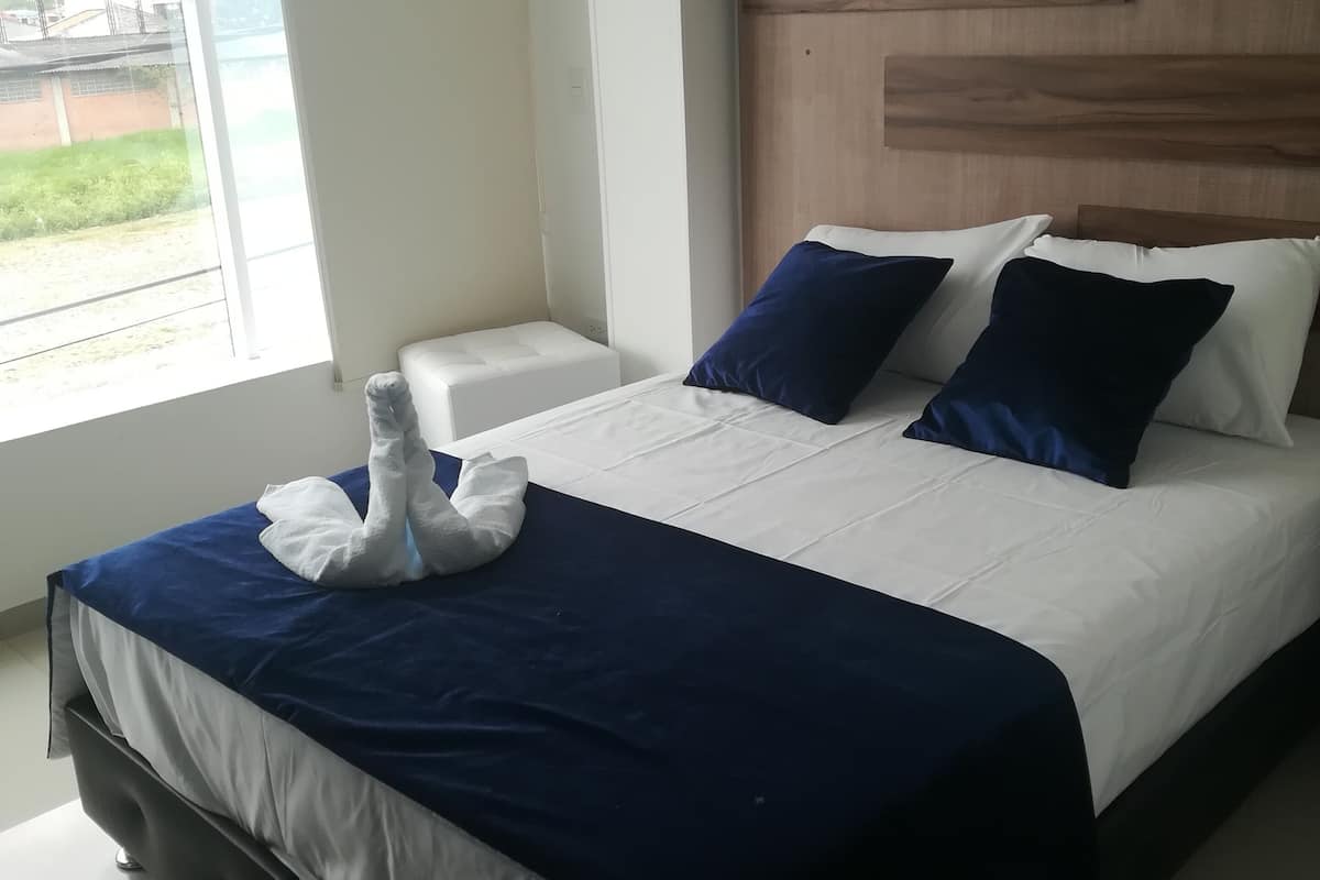 Ein Hotelzimmer mit Bett, Nachttisch und Fenster mit Blick auf Grünfläche.