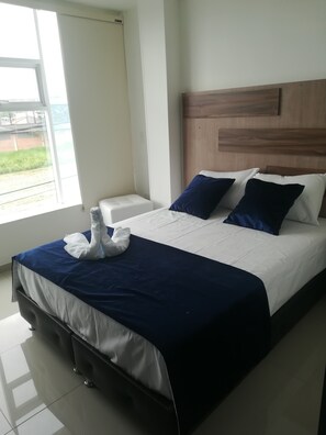 A hotel room with a bed, a nightstand, and a window with a view of greenery.