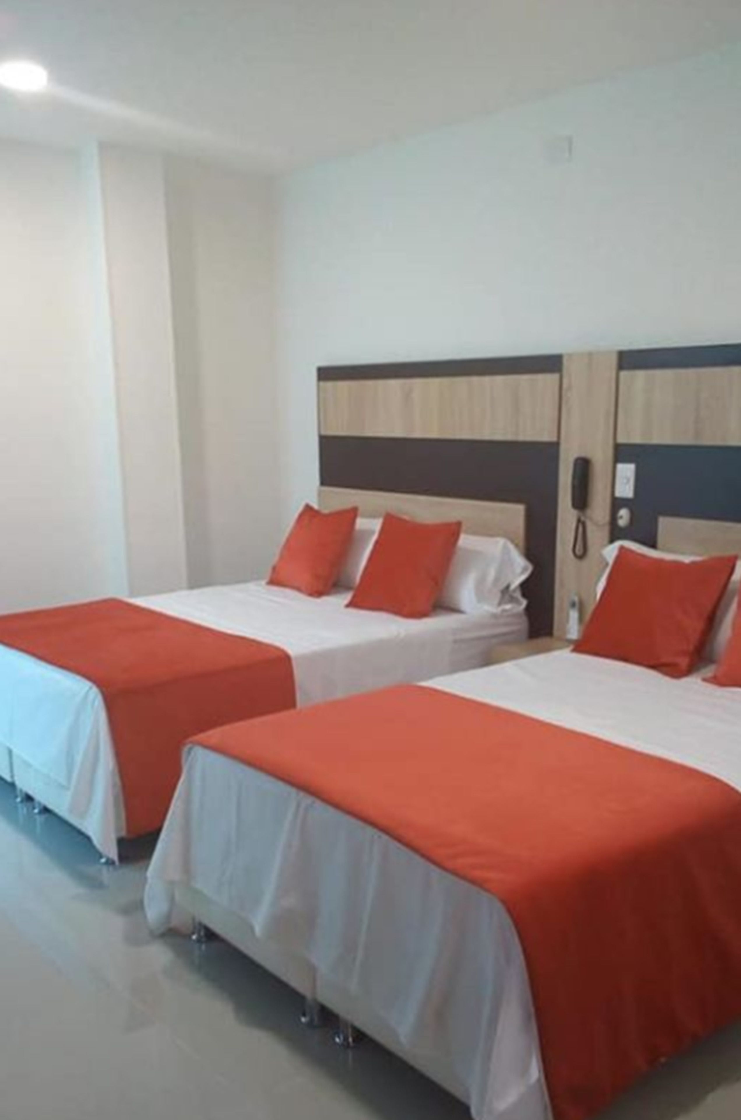 Une chambre d’hôtel avec deux lits, chacun doté d’un matelas blanc et d’une literie orange. Chaque lit est muni d’une tête de lit en bois et un téléphone est fixé au mur.