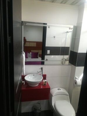 A bathroom with a white sink, red countertop, and a mirror above it. There is a white toilet next to the sink.