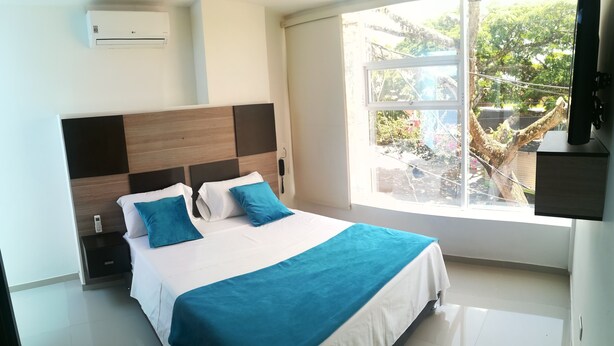 Habitación de hotel moderna con una cama grande, un cabecero de madera, un ventanal con vistas a zonas verdes y un aire acondicionado instalado.