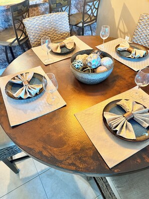 A round dining table with a textured surface, surrounded by chairs with woven cushions.