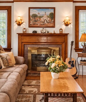 A living room with a fireplace, a sofa, a coffee table with flowers, and a guitar. - Red Fox Townhouse Private Hot Tub Near Skiing (Windham)