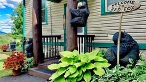 Une maison avec un porche, une pancarte de bienvenue et une statue d’ours.