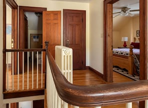 Eine Holztreppe führt zu einem Schlafzimmer mit einem Bett, einem Heizkörper und einem Deckenventilator.