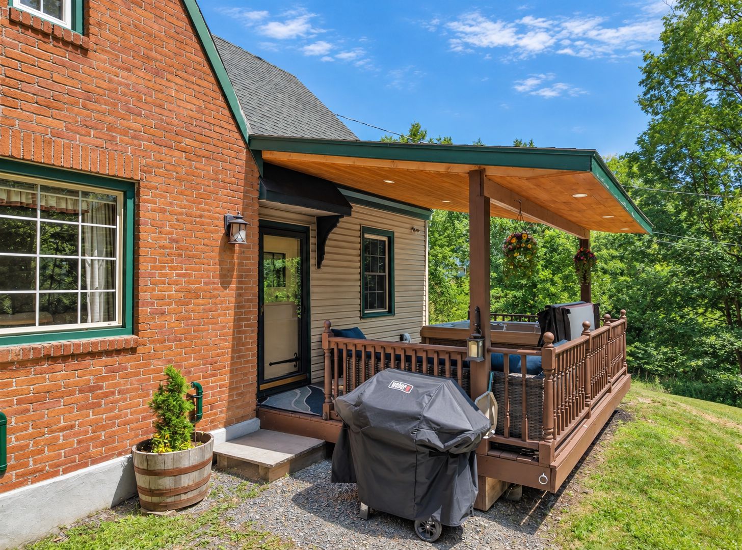 A brick house with a wooden deck, a covered porch, and a barbecue grill.