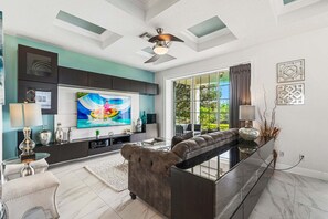 A modern living room with a sectional sofa, a flat-screen TV, and a ceiling fan. - Liberty Plaza: Private Pool, Free Water Park, Golf View, Near Disney (Kissimmee)