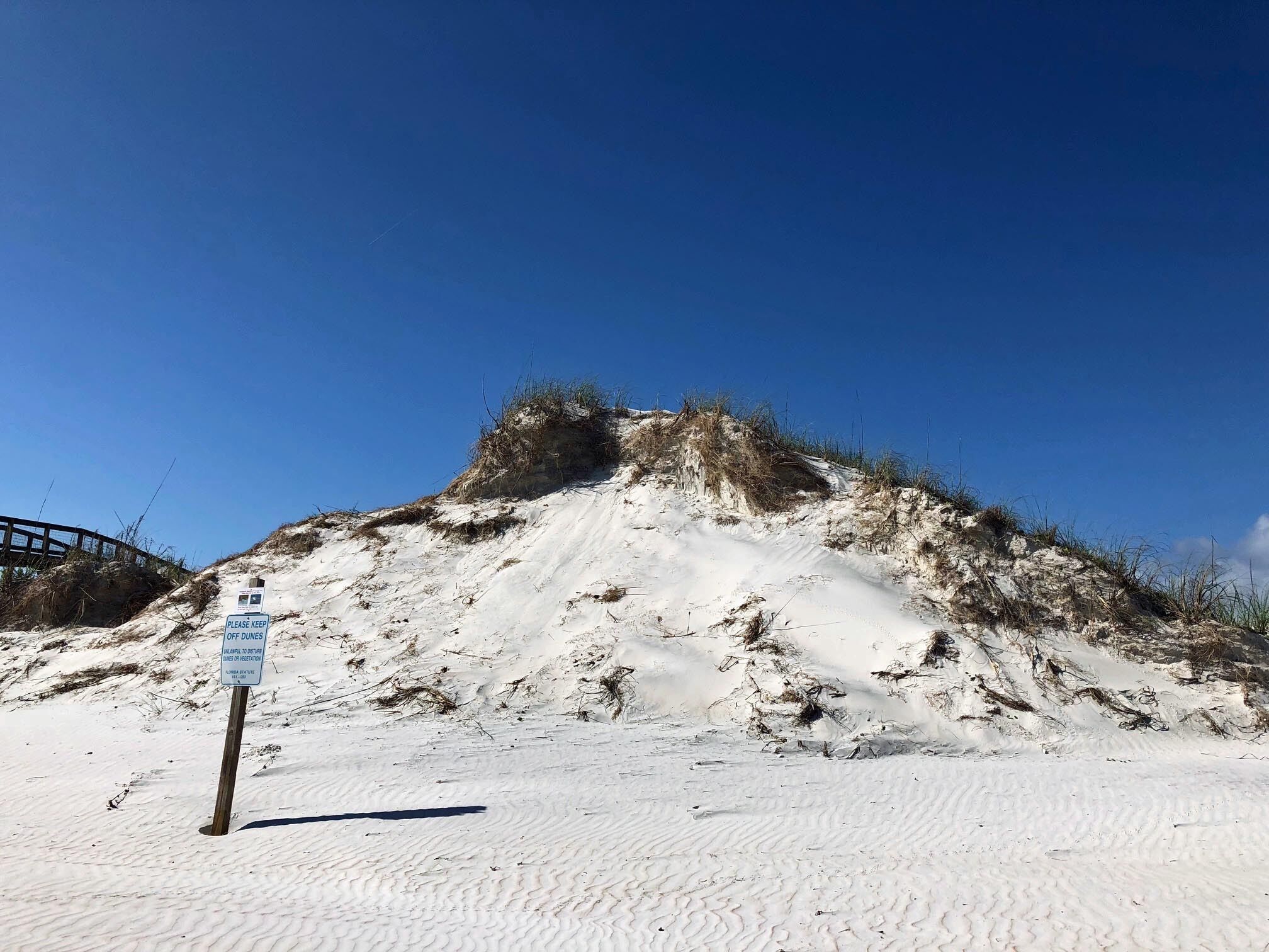 Una playa arenosa con un cartel de advertencia y una estructura de madera al fondo.
