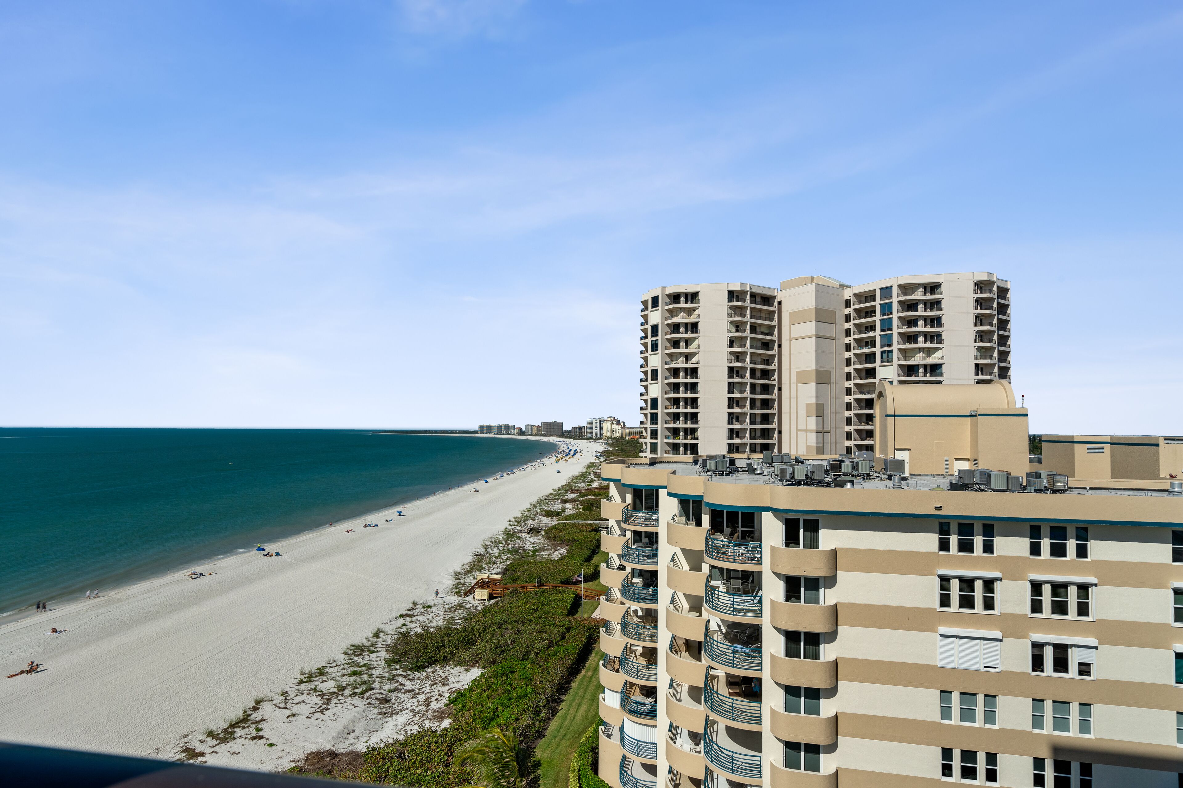 A beachfront hotel with multiple balconies, a sandy beach, and a clear view of the ocean.