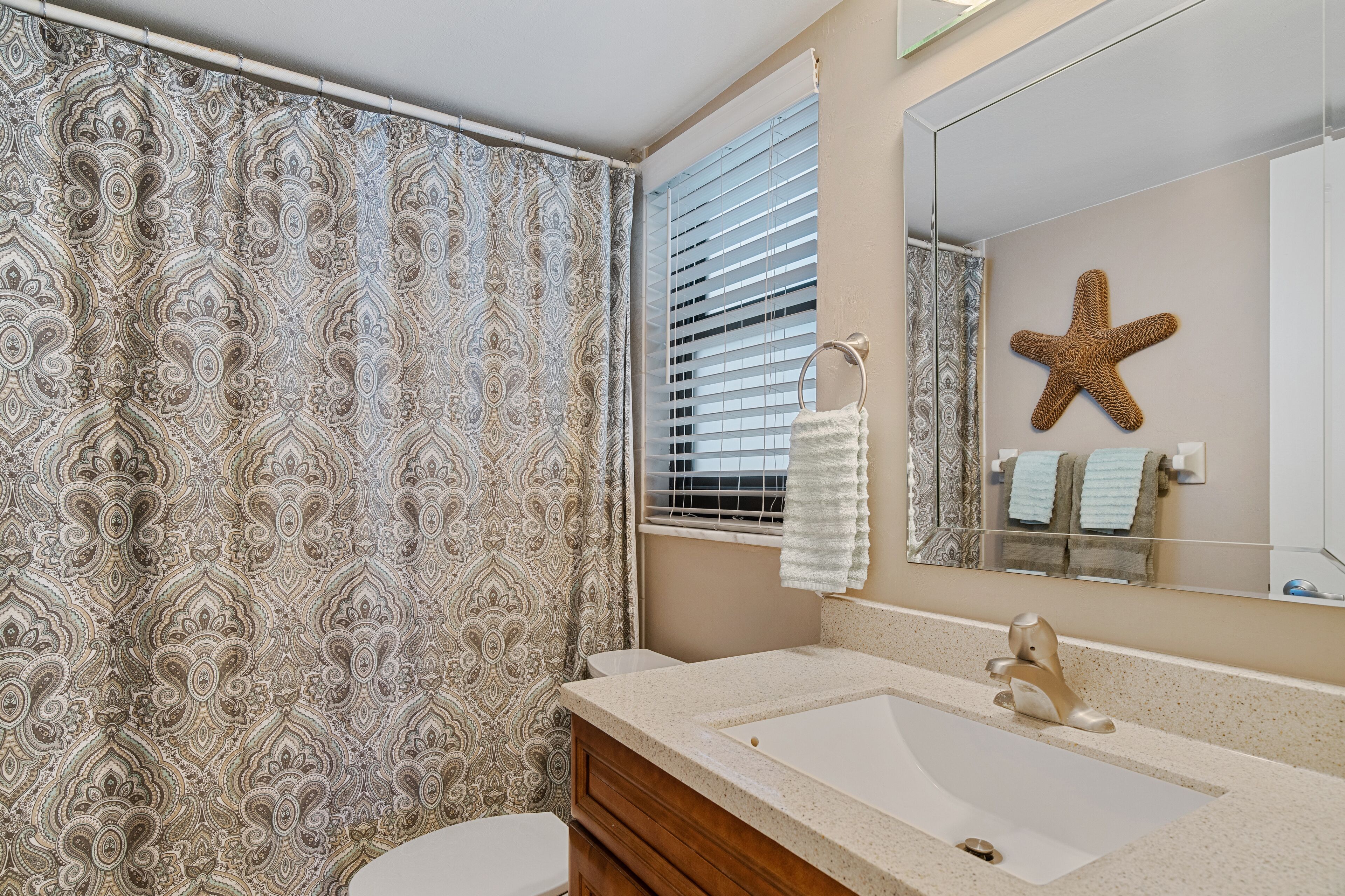 Casa de banho com cortina de chuveiro estampada, toucador com lavatório e espelho decorado com uma estrela-do-mar.