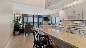 A modern kitchen with white cabinetry, a large island, and a dining area with chairs and a table. - Beautiful, updated, oceanfront views!  Gorgeous unit! (Marco Island)
