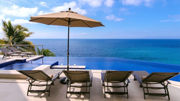A poolside area with lounge chairs and an umbrella, overlooking the ocean.