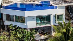 A modern multi-story house with a large swimming pool, balconies, and outdoor seating areas.