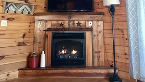 Interior acogedor de una cabaña con techo de madera, una chimenea y un televisor sobre ella, además de una lámpara junto a la chimenea.