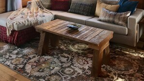 Un interior de cabaña acogedor con techo de madera, un sofá con cojines estampados, una mesita de centro y una alfombra.
