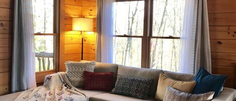 A cozy cabin interior with a wooden ceiling, a sofa with patterned cushions, a coffee table, and a rug.