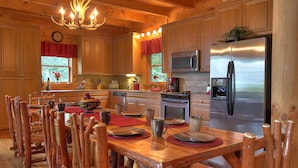 Cocina estilo cabaña de madera con comedor, candelabro y refrigerador de acero inoxidable.