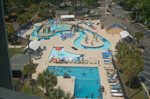 Un grand espace extérieur avec une piscine comprenant plusieurs couloirs de nage, des chaises longues et un toboggan aquatique.