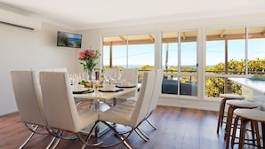 A dining area with a table set for four, white chairs, and a view of the outdoors. - Marilyn's - 180 degree views of Jervis Bay (Callala Beach)