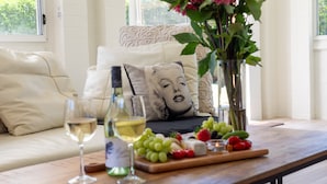 A cozy seating area with a sofa, a table with wine glasses, a bottle, and a fruit platter. - Marilyn's - 180 degree views of Jervis Bay (Callala Beach)