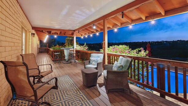 A covered outdoor deck with wooden flooring, wicker furniture, and a view of a body of water at dusk. - Spectacular Views! Heated Pool. Game Room. Private. Spacious. (Fountain Hills)