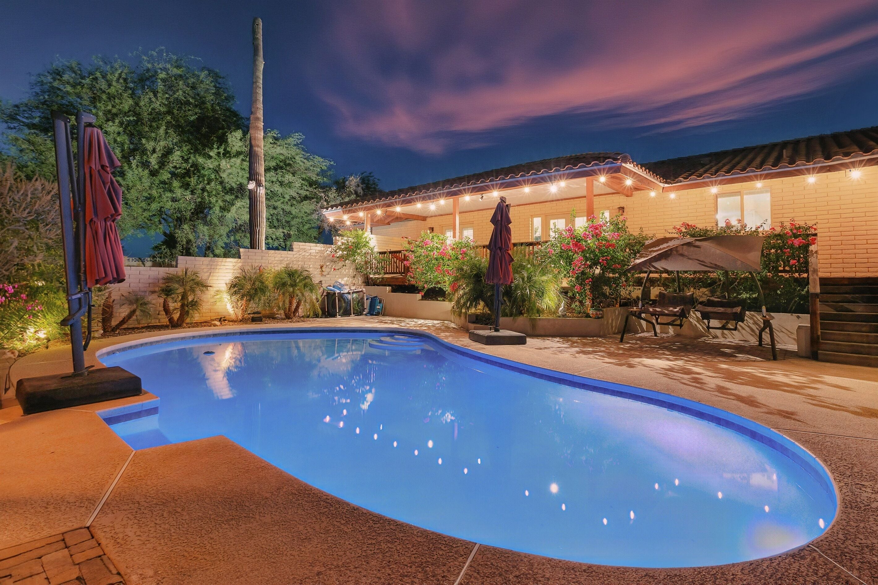 Une piscine entourée d’une terrasse en briques, elle-même bordée d’un espace extérieur aménagé avec des meubles de jardin et des guirlandes lumineuses.