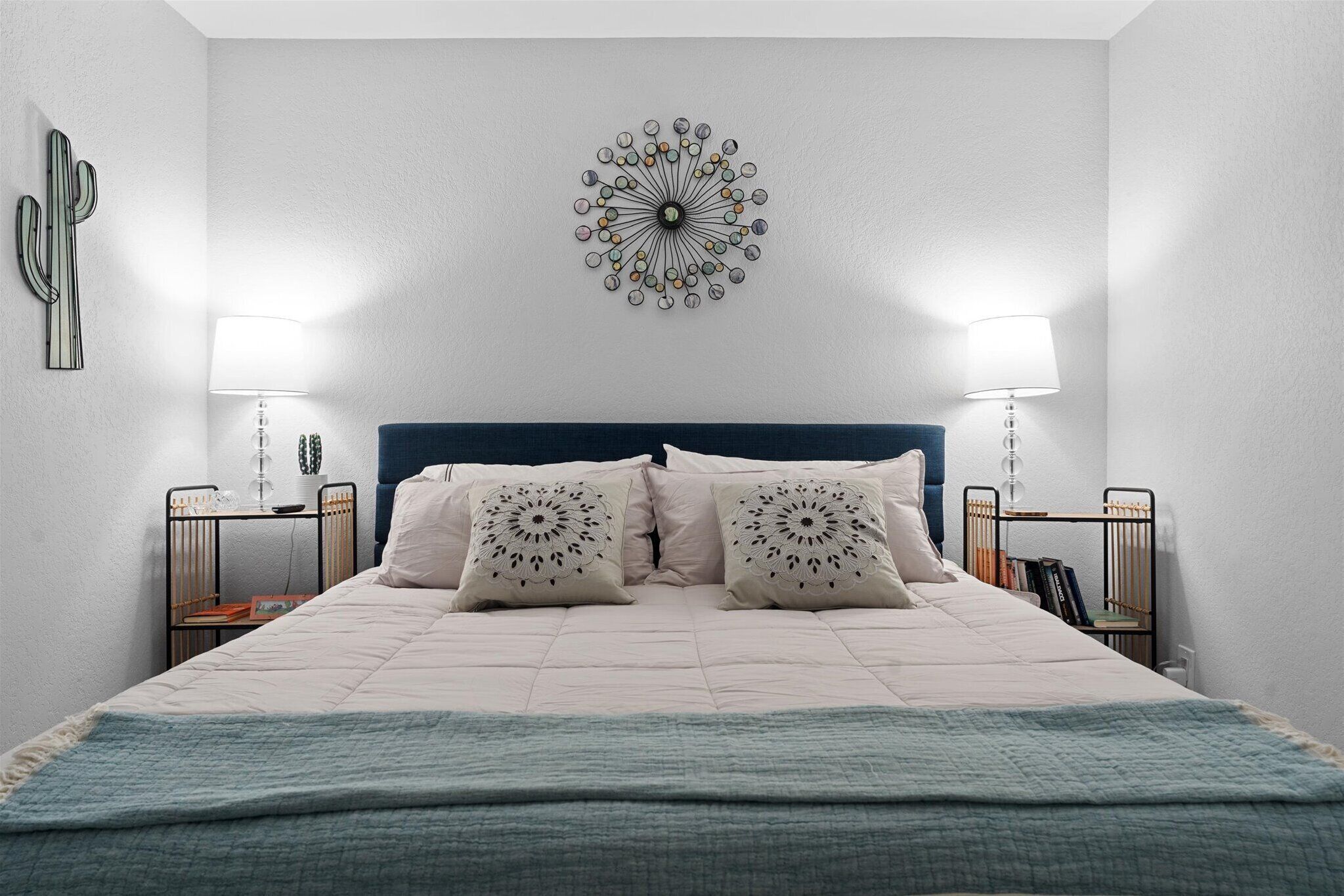 Een slaapkamer met een bed, twee nachtkastjes, een wandlamp en een cactus decoratie.