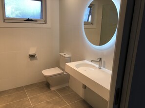 A modern bathroom with a toilet, sink, and a mirror with a circular light. - Golfview Lorne - For all seasons (Lorne)