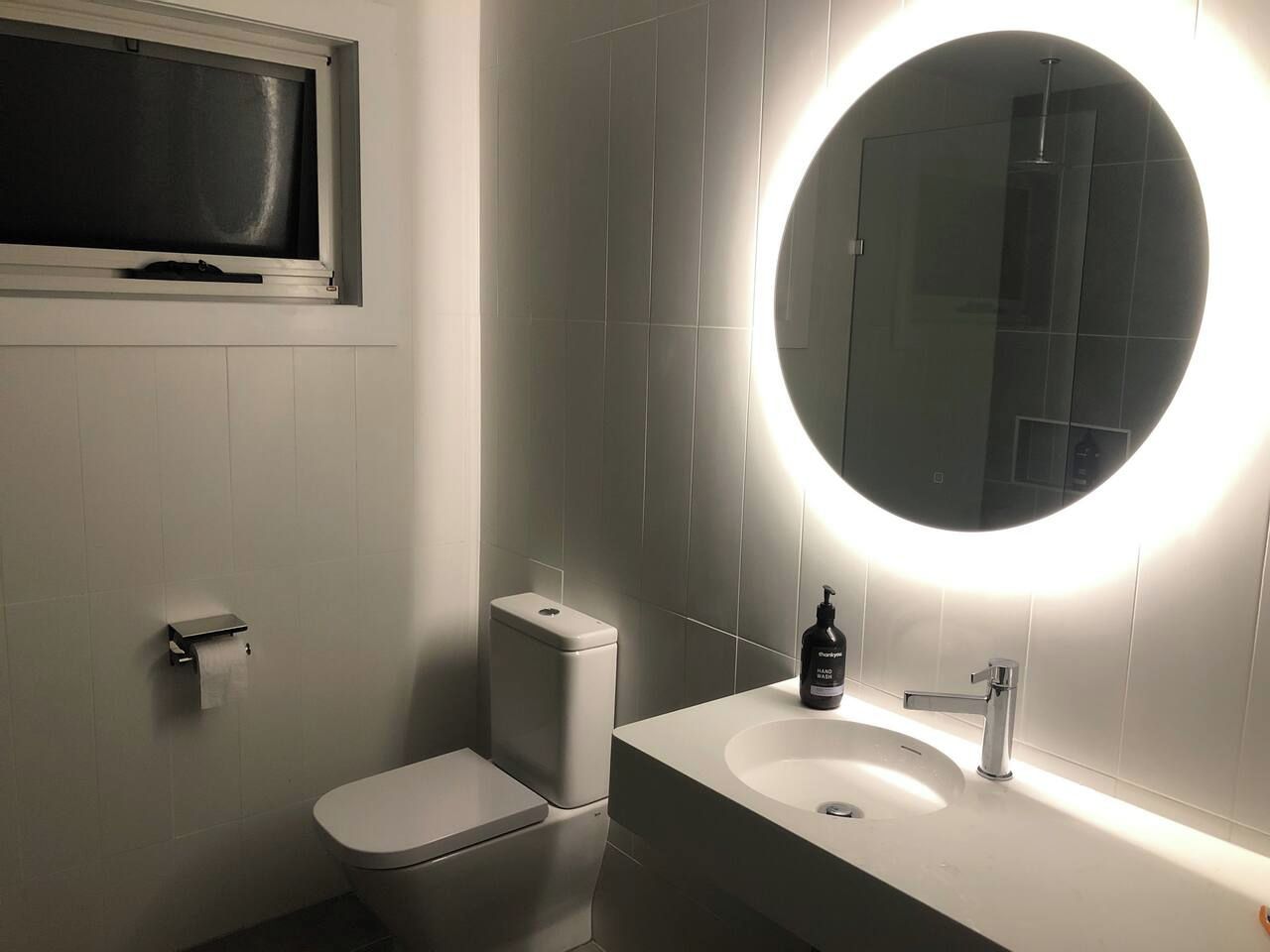 A modern bathroom with a toilet, bidet, and a sink with a round mirror.