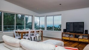A modern living room with a white sofa, a dining table with chairs, a TV, and a bookshelf. - Golfview Lorne - For all seasons (Lorne)