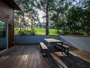 An outdoor deck with wooden flooring and benches, overlooking a grassy area with trees. - Golfview Lorne - For all seasons (Lorne)
