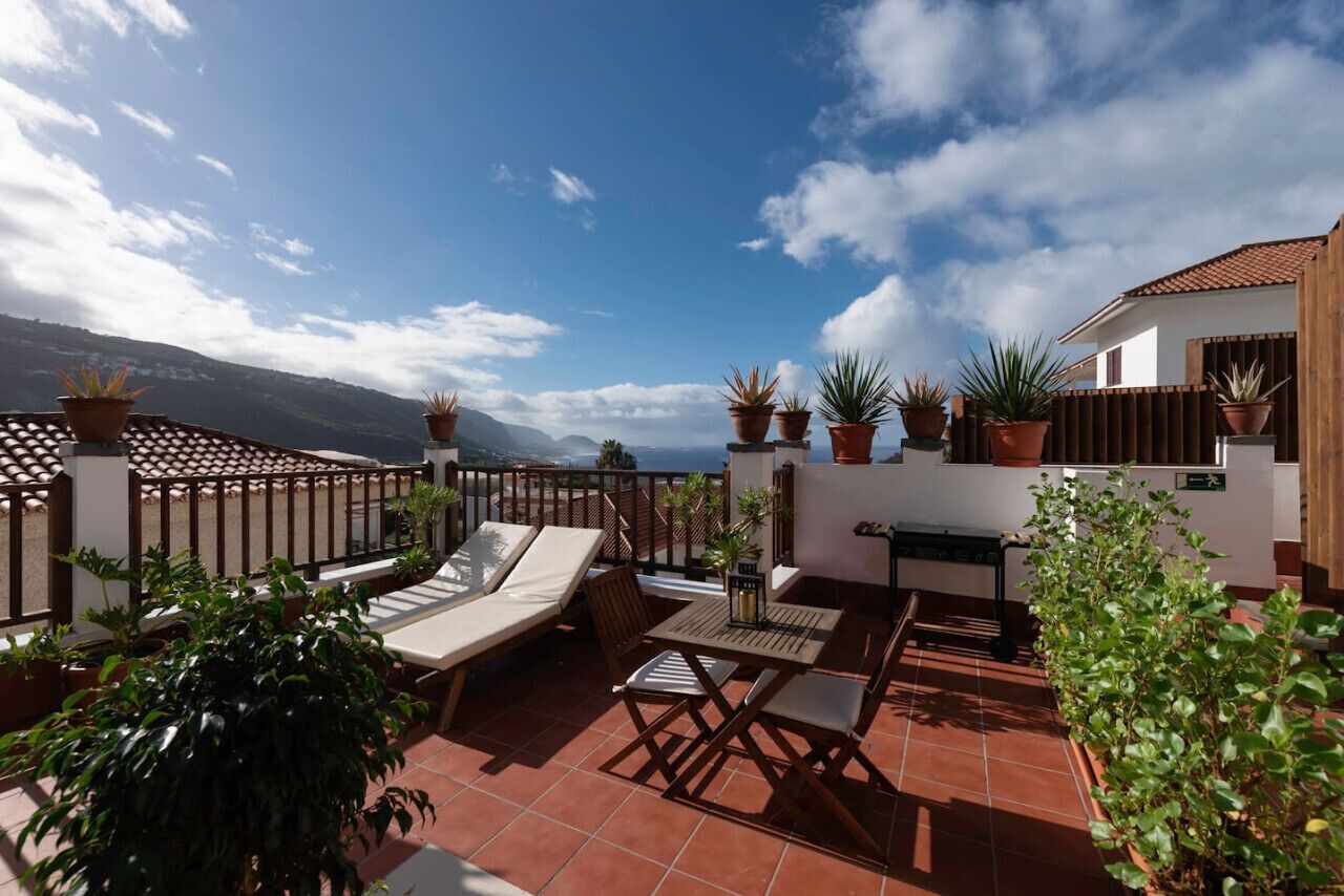 Terraza en la azotea con vistas a las montañas, amueblada con sillones y una mesa.