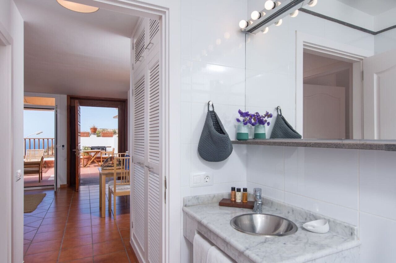 Un baño moderno con lavamanos de mármol, un espejo con iluminación y vistas al patio exterior.