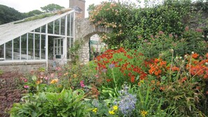 Une serre dotée d’une arche en pierre, entourée d’une variété de fleurs et de plantes aux couleurs vives.