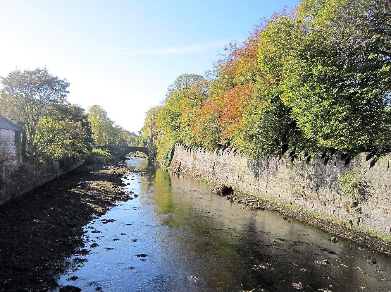 A narrow waterway flanked by stone walls and trees with autumn foliage.