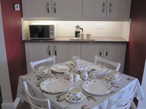 A dining area with a table set for four, white chairs, a microwave, and a coffee maker on the counter. - The Glenarm Lookout, Causeway Coast & Glens (Glenarm)