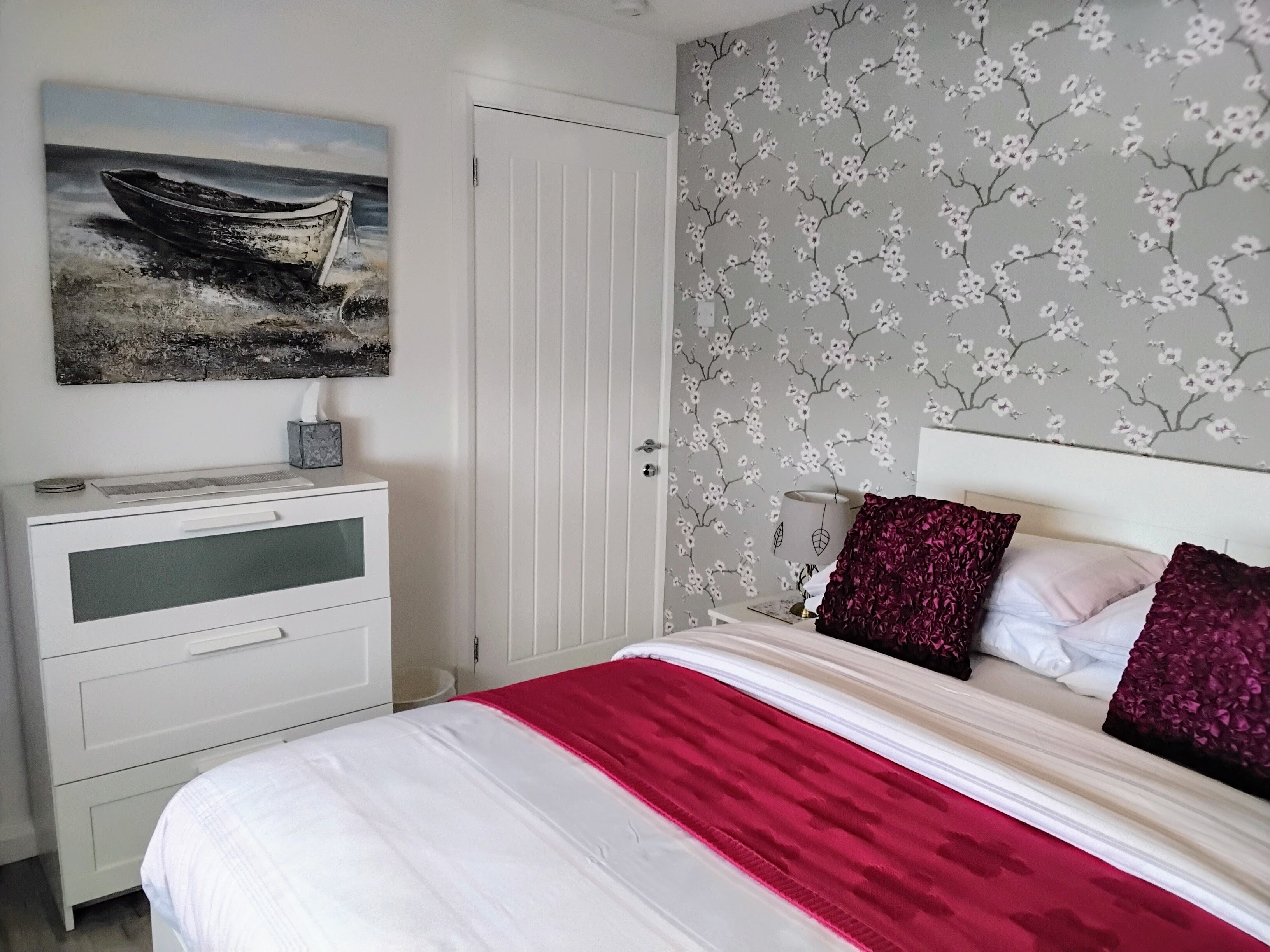 A bedroom with a bed, a nightstand, a desk, and a door.