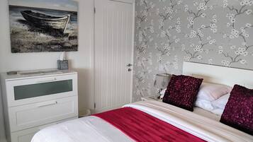 A bedroom with a bed, a nightstand, a desk, and a door.