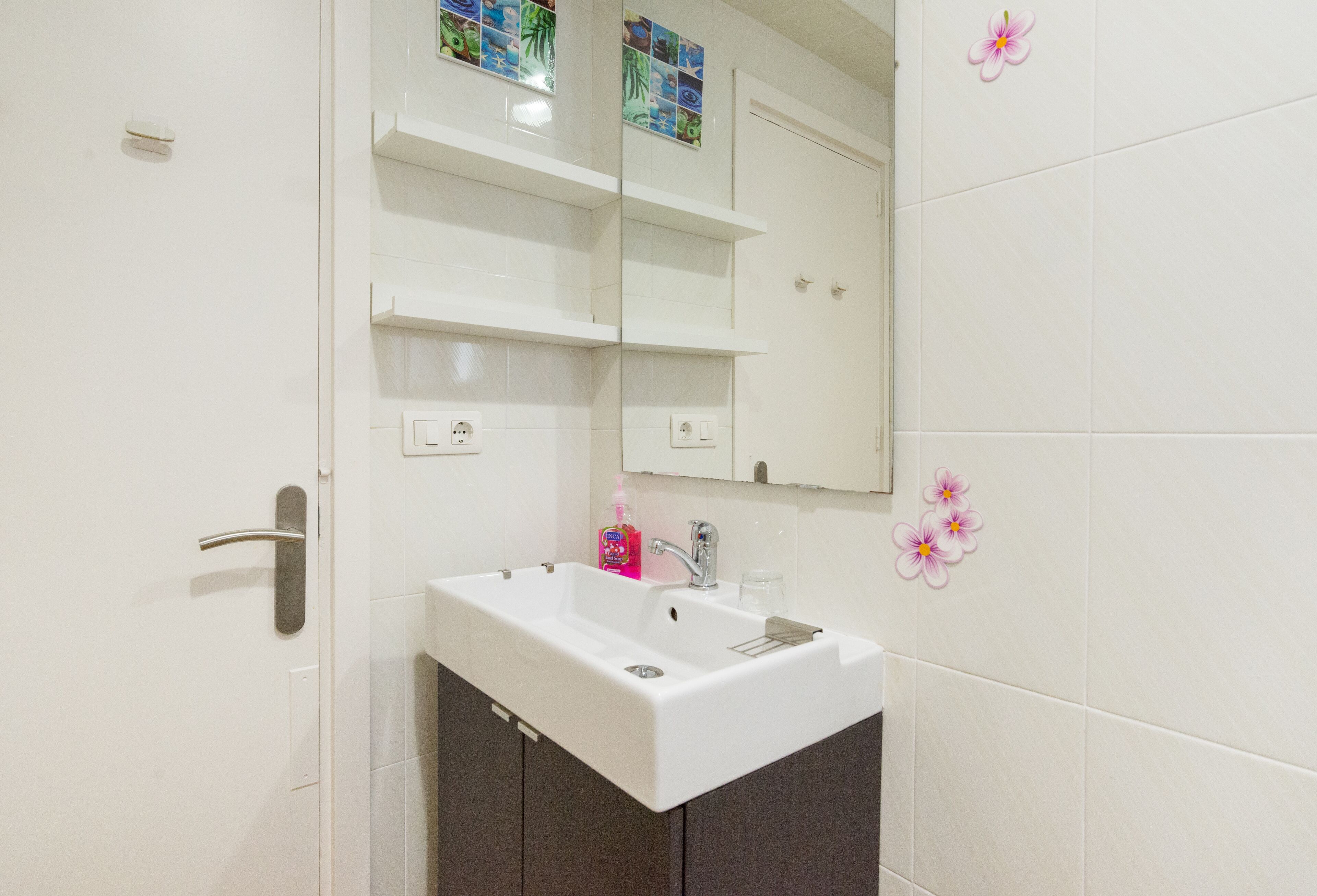 Un bany amb un lavabo blanc, mobles fosc, un mirall i rajoles decoratives.