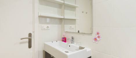Un bany amb un lavabo blanc, mobles fosc, un mirall i rajoles decoratives.