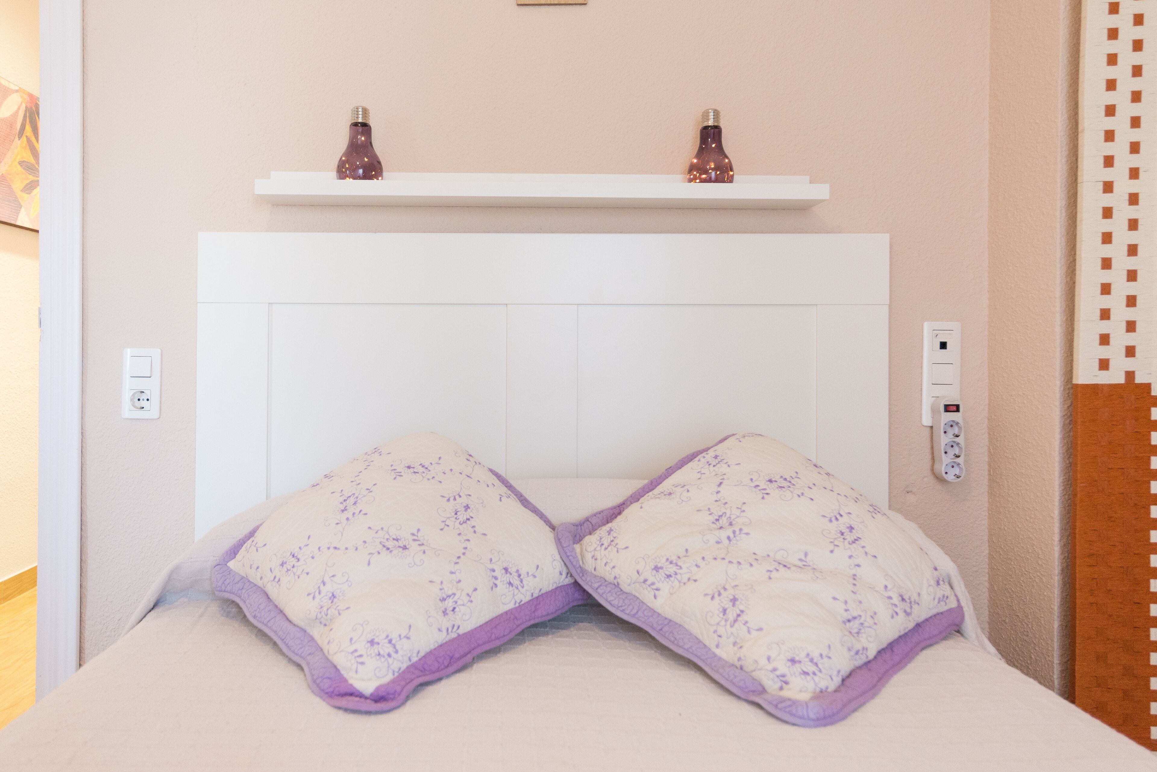 A bed with a headboard, two bedside lamps, and a wall socket.