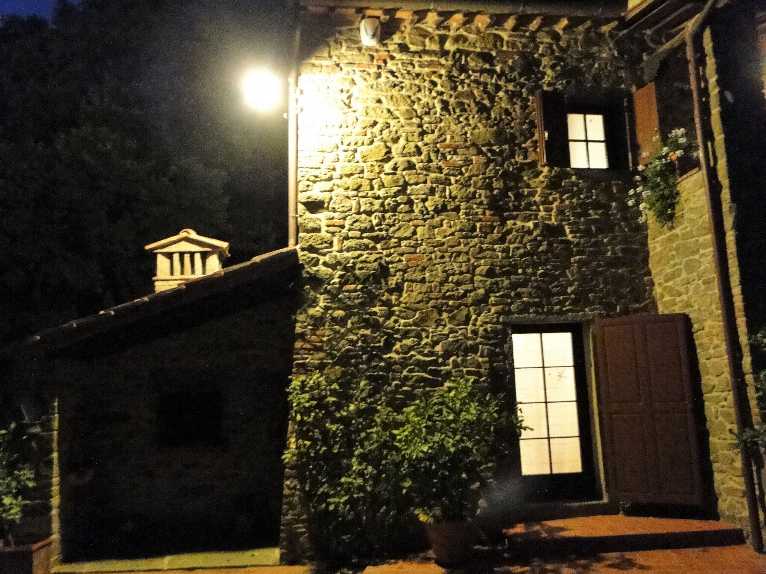 A stone building with a small window and a door, illuminated by a single light source.