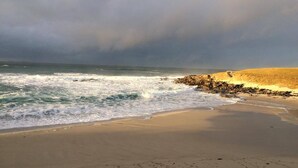 A beach with waves crashing onto the shore, a sandy beach, and a rocky outcrop in the background.