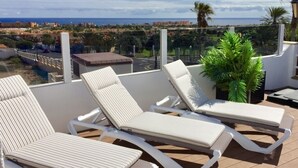 Una terrazza con tre lettini, una pianta in vaso e vista sulla costa.