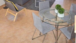 Un soggiorno moderno con un divano grigio, due lampade da terra, un tavolino da caffè in vetro e un tavolo da pranzo rotondo in vetro con sedie.