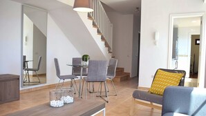 Un soggiorno moderno con zona pranzo, una scala e vista su un'altra stanza.