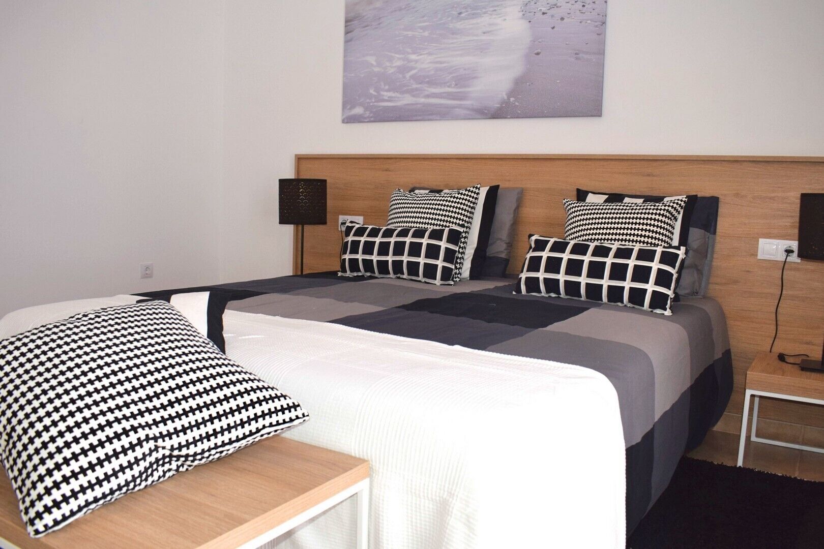 Une chambre à coucher bien rangée, avec un lit, des oreillers, une table de chevet et une lampe fixée au mur.