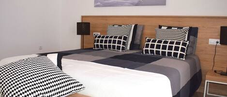 Une chambre à coucher bien rangée, avec un lit, des oreillers, une table de chevet et une lampe fixée au mur.