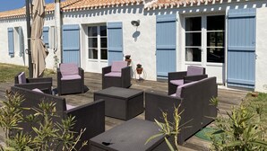 Een terras met rieten meubilair en een wit gebouw met blauwe luiken.