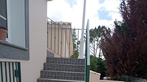 A set of stone steps leading up to a building entrance, flanked by a metal fence and a paved area with a stone border. - Guest Apartment in Santana (Santana)